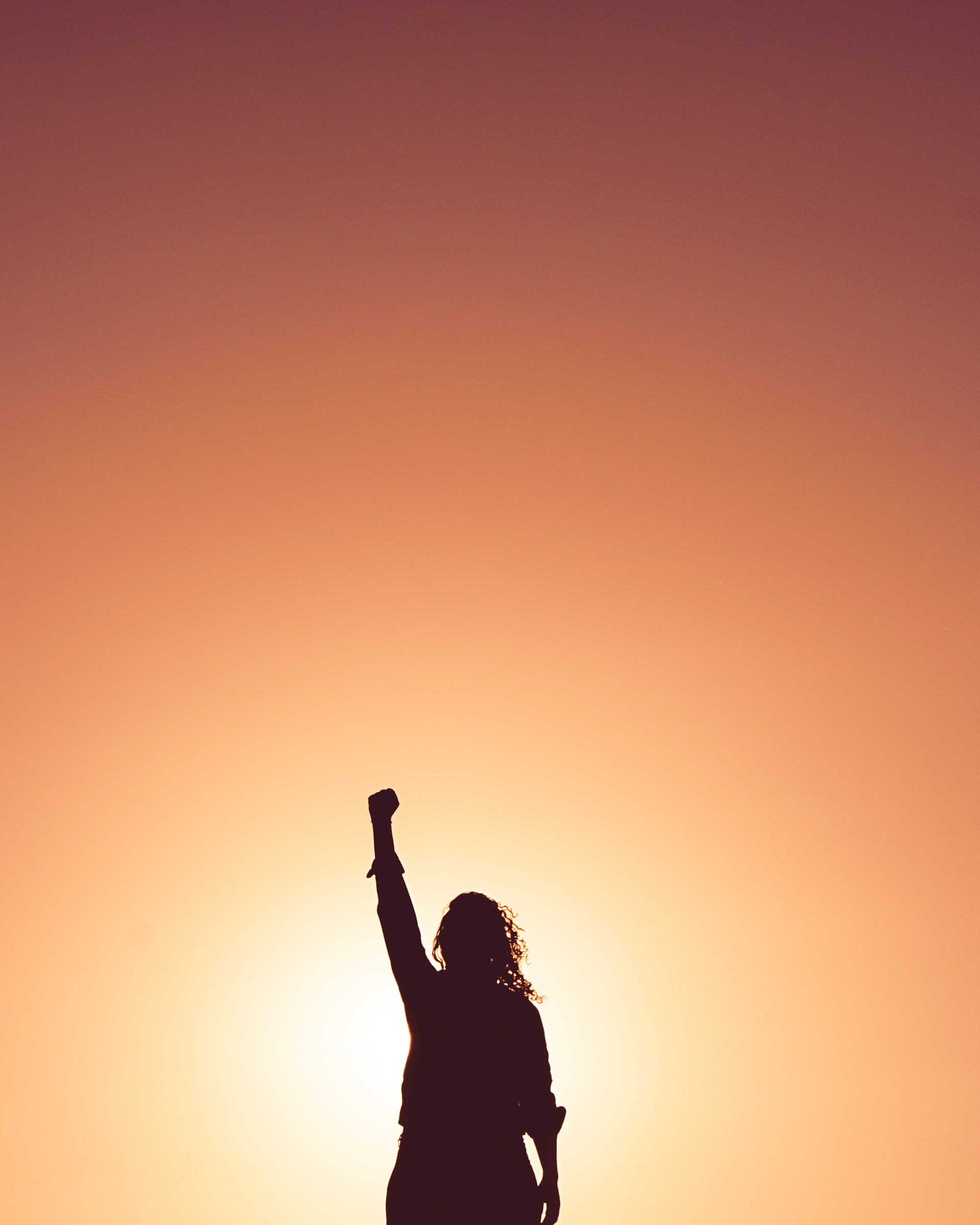image of woman standing against orange background with one hand in the air