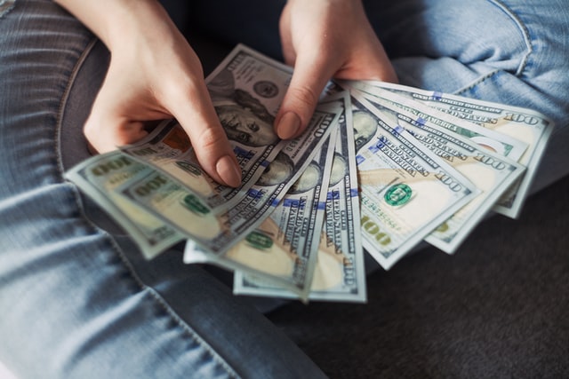 Close up image of a woman's hands holding one hundred dollar bills in her hand